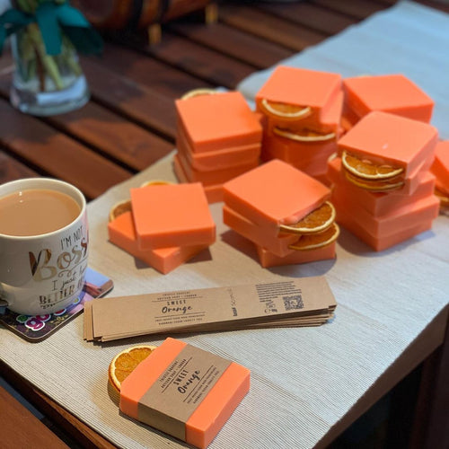 Sweet orange soap, solid orange bar with dried fruit slice decoration. Bars are being hand wrapped in recycled brown craft paper sleves