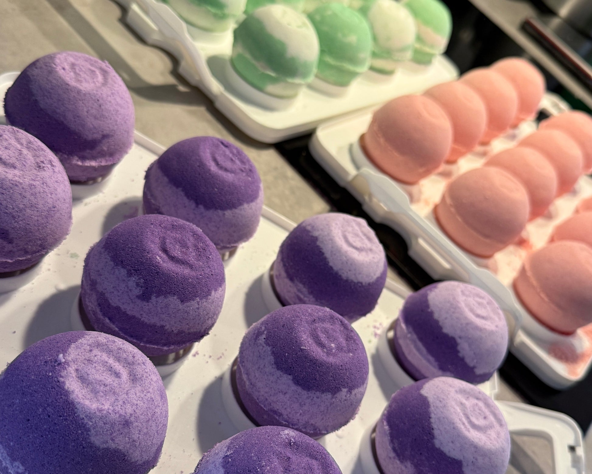 Bath bombs in various colors including purple, green, and pink on trays.