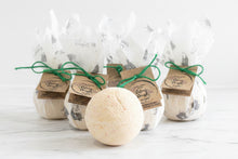 Load image into Gallery viewer, Pale orange bath bomb with beautifully packaged bath bombs in the background 
