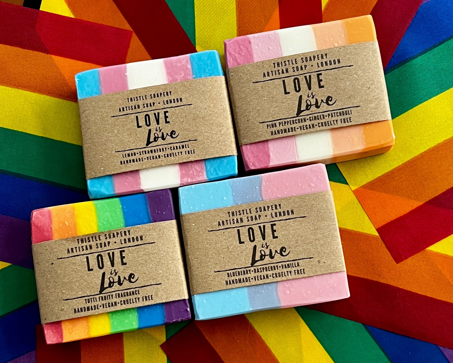 Four soap bars with 'Love is Love' packaging on a colorful pride flag background
