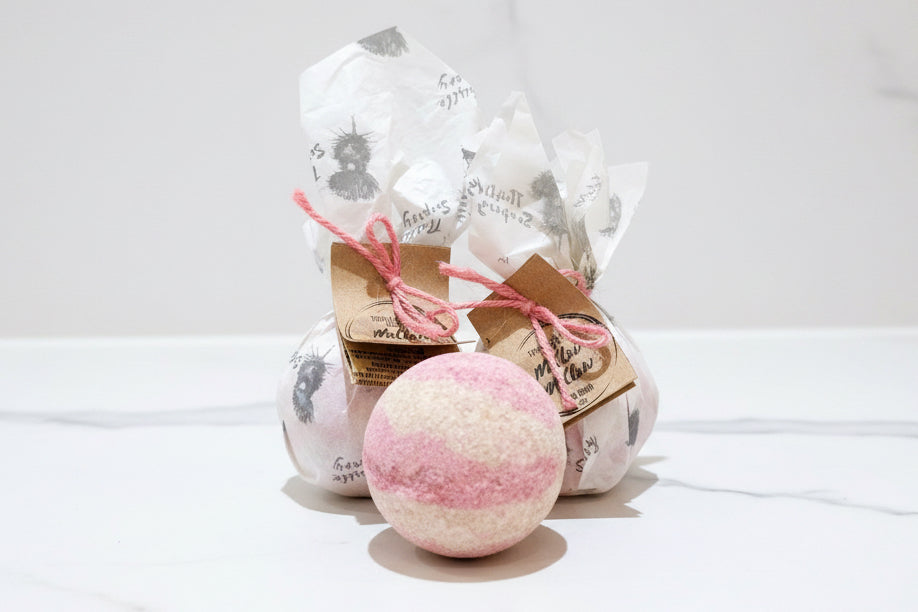 Pink and cream bath bomb with beautifully packaged bath bombs in the background 