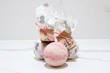 Load image into Gallery viewer, Pink and cream bath bomb with beautifully packaged bath bombs in the background 
