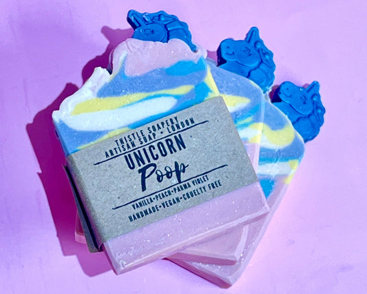 Unicorn poop soap with a pink, blue, yellow and white swirl pattern and unicorn shaped topper on a purple background